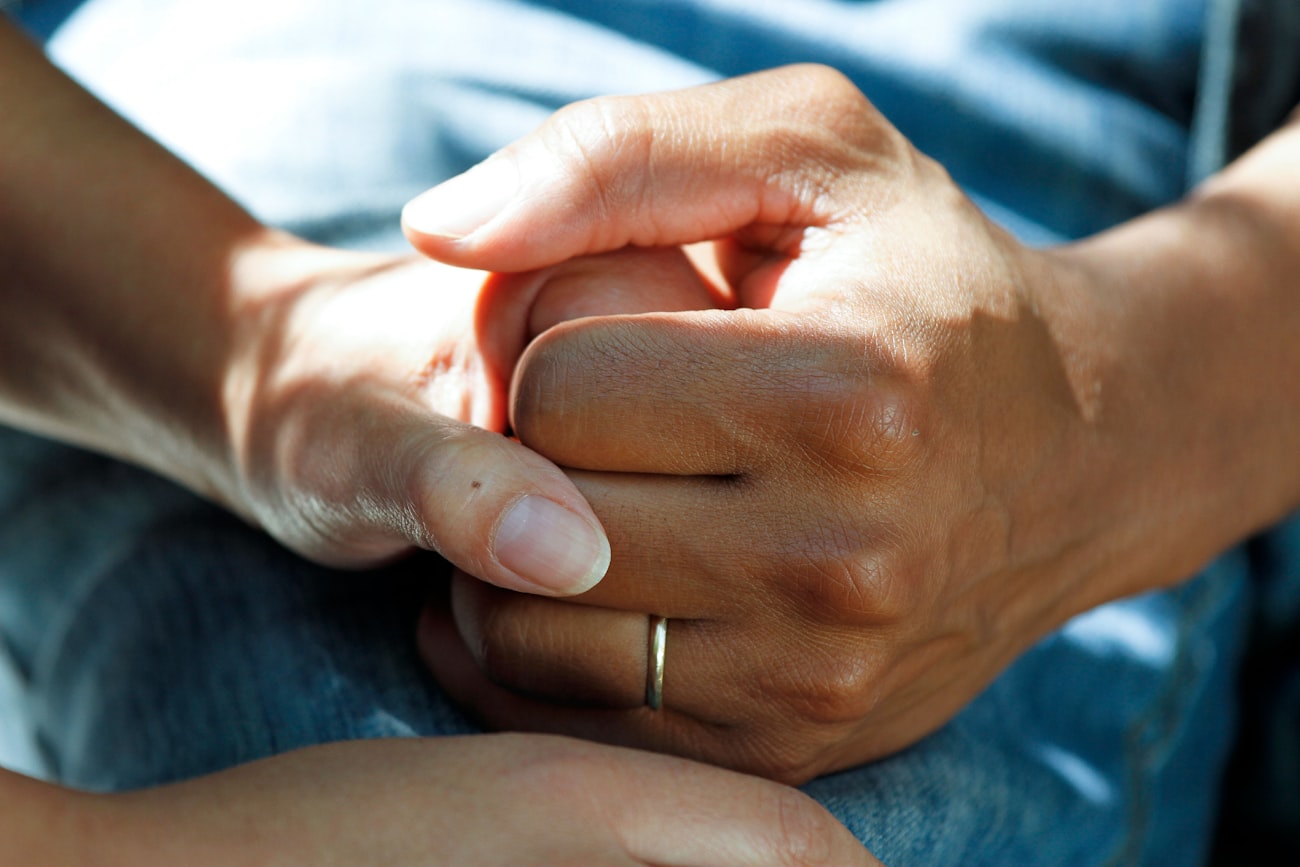 A caregiver's hands gently holding an older adult's hand
